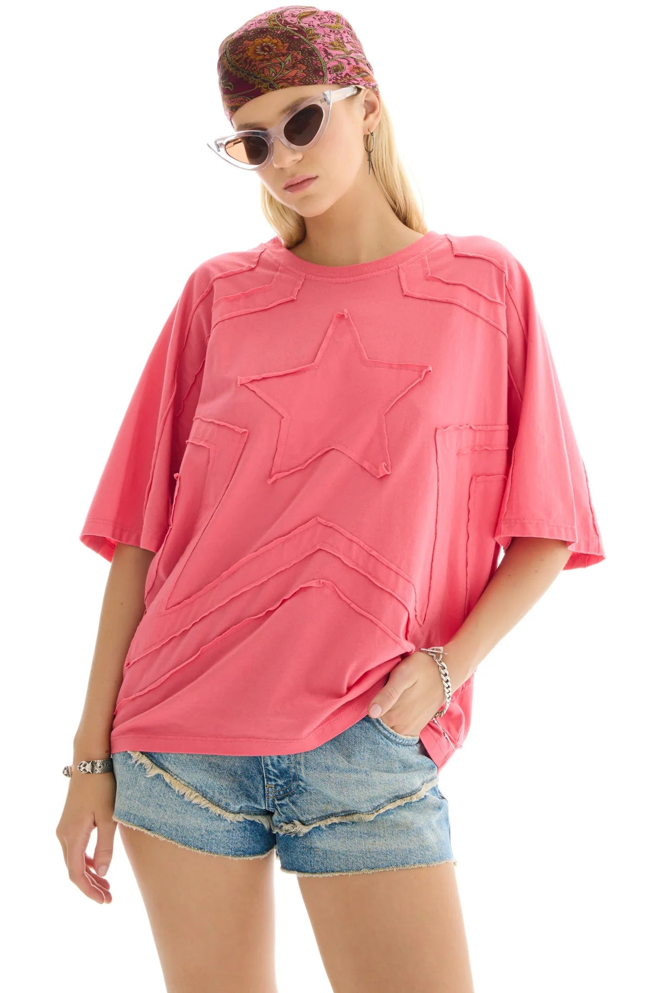 Woman wearing a pink star-shaped t-shirt and denim shorts on a white background