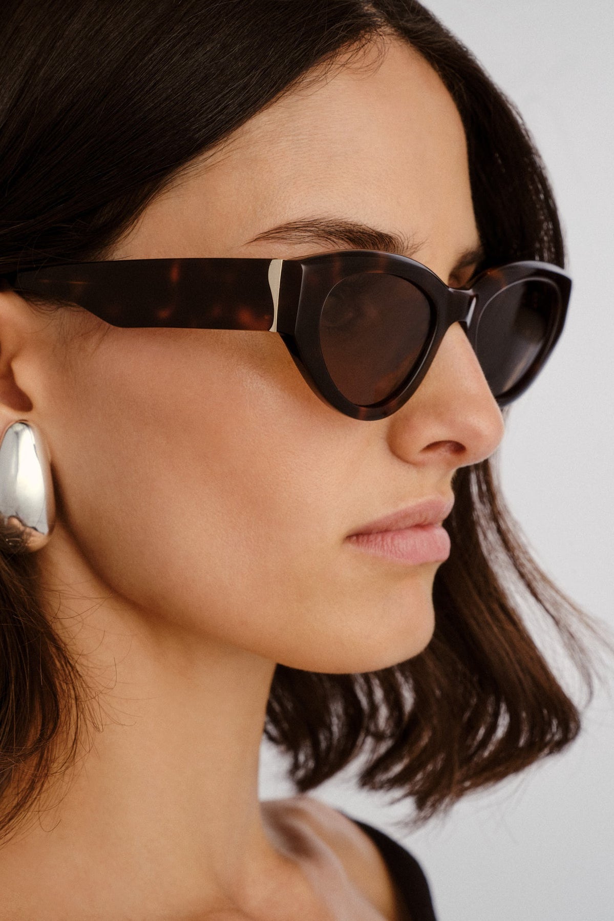 Woman wearing tortoiseshell sunglasses with a neutral background