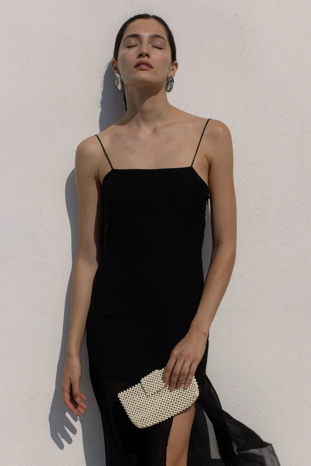 Woman wearing a black slip dress holding a pearl clutch against a light background
