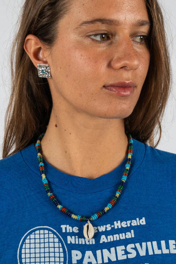 Woman wearing a blue shirt with text and a colorful beaded necklace against a white background