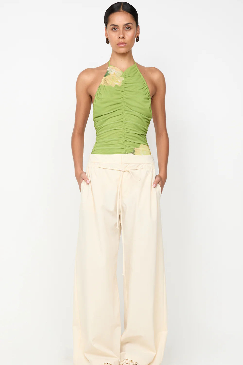 Woman wearing a green halter top and white pants on a white background