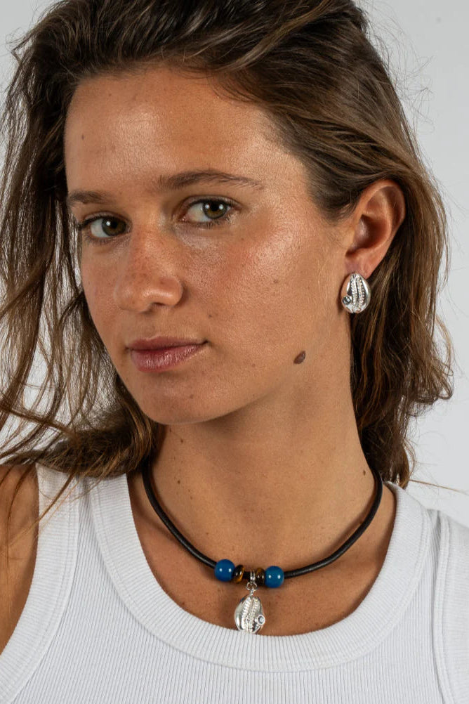 Woman wearing a white tank top with a necklace and earrings against a plain background