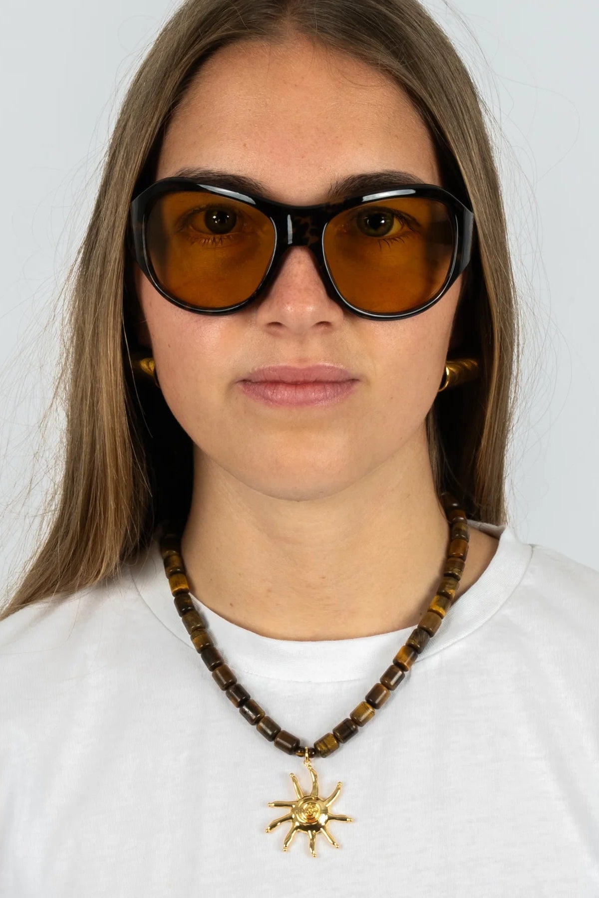 Person wearing sunglasses and a necklace with a star pendant on a white background